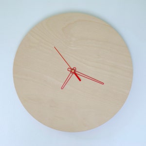 May include: A simple, round, wooden clock with red hands. The clock face is made of light wood and has a subtle grain pattern.