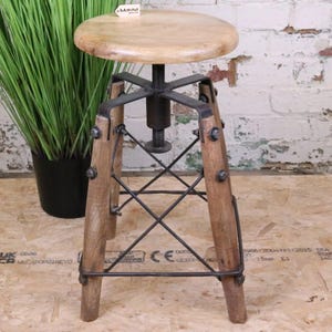 May include: A wooden adjustable stool with a round seat and a metal base. The stool has a light brown seat and dark brown legs. The metal base has a cross-hatch design. The stool is designed for indoor use.