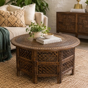May include: A round, dark brown wooden coffee table featuring intricate hand-carved floral patterns on the top surface and a lattice-style openwork design on the base. The table edge is accented with a delicate white inlaid dot pattern.