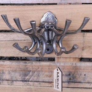 May include: A silver metal coat rack with multiple hooks. The rack is mounted on a wooden wall. The rack has a tag that says "Maravi" and "Made in the UK".
