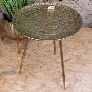 May include: A round, brass-colored side table with three slender legs. The tabletop has a textured, crackled pattern in shades of green and gold. The table is approximately 20 inches in diameter.