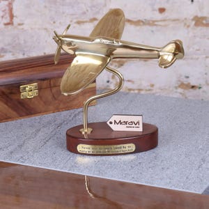 May include: A gold-colored brass model of a Spitfire airplane on a wooden base. The base has a plaque with the quote "Never was so much owed by so many to so few - Sir Winston Churchill".