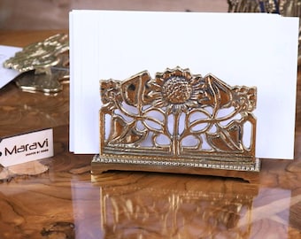 Puede incluir: Un porta tarjetas de visita de metal dorado con un diseño de girasol. El porta tarjetas está sobre una superficie de madera.