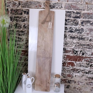 Könnte beinhalten: Ein langes, rechteckiges Holzbrett zum Servieren mit einer natürlichen Holzoptik. Das Brett hat oben einen Griff und ein kleines Schild mit der Aufschrift "MASON".