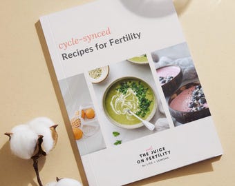 May include: A white cookbook with the title "cycle-synced Recipes for Fertility" by "The Juice on Fertility by Life + Lemons". The cover features photos of green and pink smoothies in bowls.