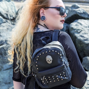 Può includere: Zaino nero in similpelle con borchie argentate e un tirare zip a forma di teschio. Lo zaino ha una piccola tasca frontale e spalline regolabili.