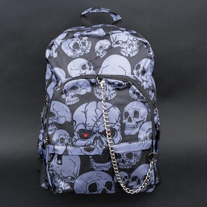 Pode incluir: Uma mochila preta com uma corrente prateada e um padrão de caveiras. As caveiras são em tons de cinza e branco.