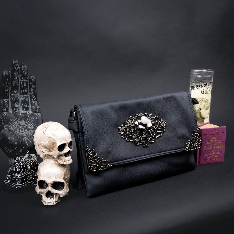 Gothic black vegan leather bag by CHOK GothX with a silver skull and rose motif, styled with dark props like a spellbook and skulls.