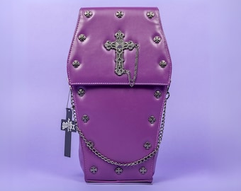 Puede incluir: Bolso morado con forma de ataúd con una cruz decorativa y detalles de cadena. El bolso presenta tachuelas metálicas y una etiqueta que dice "gothx". El bolso tiene una correa de cadena y un cierre de solapa.