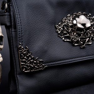 Close-up of metal floral skull emblem and corner detailing on CHOK GothX gothic black vegan leather bag clip close flap.