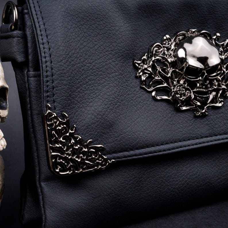 Close-up of metal floral skull emblem and corner detailing on CHOK GothX gothic black vegan leather bag clip close flap.