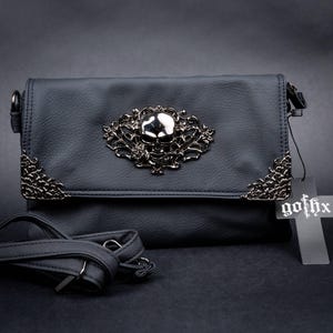 Gothic black vegan leather bag by GOTHX with a silver skull and rose motif, styled on a dark black background. Showing the cross tag and the detachable adjustable strap.