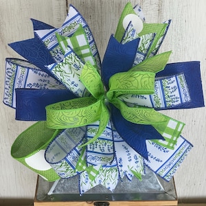 May include: A green and blue bow with a white and blue floral pattern. The bow is made of ribbon and is tied in a knot. It is a decorative item that can be used for a variety of purposes.