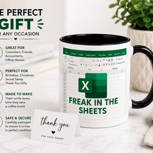 May include: White ceramic mug with a black interior and handle. The mug features an Excel spreadsheet design with the text "FREAK IN THE SHEETS" and the Excel logo. A small card reads "thank you" with a heart.