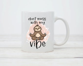 Może przedstawiać: Biały kubek ceramiczny z medytującym leniwcem w różowym wzorze akwarelowym. Na kubku nadrukowany jest tekst "don't mess with my vibe".