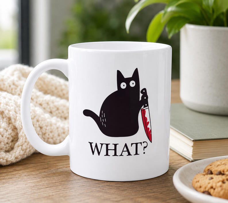 May include: A white ceramic mug featuring a black cat illustration holding a knife with red blood stains on the blade. Below the cat, the word WHAT? is printed in black capital letters. The mug has a curved handle and a smooth, glossy finish.