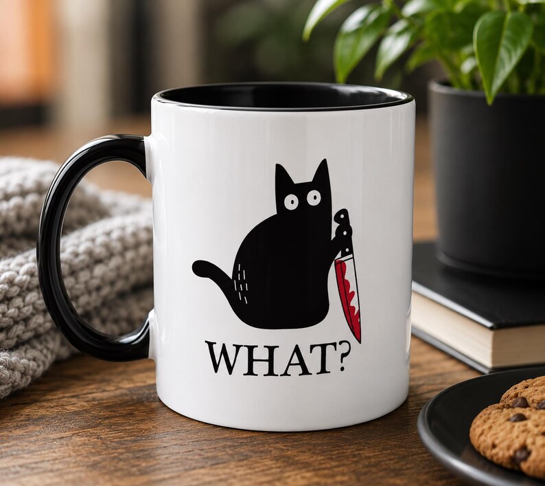 May include: A white ceramic mug with a black handle and interior. The front features a graphic of a black cat with wide eyes holding a knife with red blood stains on the blade. Below the cat, the word WHAT? is printed in black capital letters.