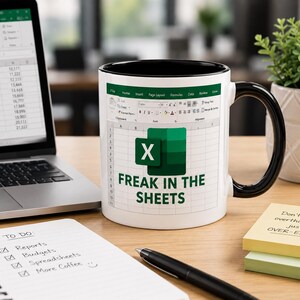 May include: White ceramic mug with a black handle and rim, featuring an Excel spreadsheet design and the text "FREAK IN THE SHEETS." A laptop, notepad, pen, and sticky notes are also visible.