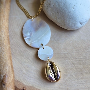 May include: A gold chain necklace with three pendants. The top pendant is a large, iridescent, oval-shaped shell. Below it is a smaller, round, white pendant. The bottom pendant is a gold-colored, shell-shaped charm.