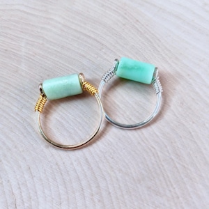 May include: Two rings with a light green stone wrapped in wire. One ring is gold and the other is silver.
