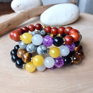 May include: A stack of bracelets with various colored beads, including yellow, white, purple, black, brown, and tiger's eye.