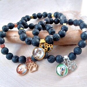 May include: Three black lava stone bracelets with gold and silver accents. Each bracelet has a charm with a photo of a dog and a paw print.