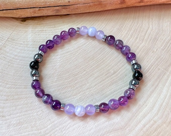 May include: A purple amethyst and blue agate beaded bracelet with silver spacers. The bracelet is on a wooden surface.