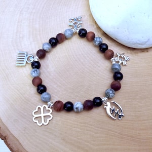May include: A beaded bracelet featuring alternating matte brown, glossy black, and grey marbled beads. The bracelet is accented with five silver-toned metal charms, including a four-leaf clover, a comb, and three distinct Adinkra-style symbols.
