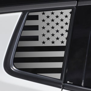 Könnte beinhalten: Ein schwarz-weißes amerikanisches Flaggen-Aufkleber auf einem Autofenster. Die Flagge hat die Form eines Rechtecks und befindet sich auf der Heckscheibe des Autos.