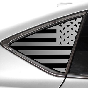 May include: A black and white American flag decal on a car window. The flag is in the shape of a triangle and is placed on the back window of the car.