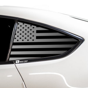 May include: A white car with a black and grey American flag decal on the rear quarter window. The decal is on the passenger side of the car. The decal has the words "Bogar Tech Designs" in white text on a black background.