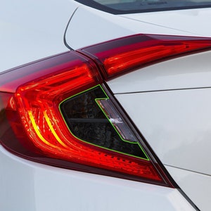 K&ouml;nnte beinhalten: Nahaufnahme eines roten R&uuml;cklichts an einem wei&szlig;en Auto. Das R&uuml;cklicht hat ein schwarzes Geh&auml;use und eine klare Linse. Das R&uuml;cklicht ist eingeschaltet und die Bremslichter leuchten.