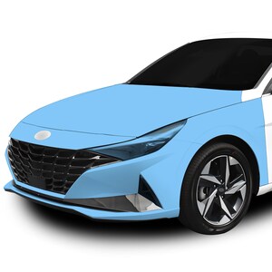 Op de afbeelding: Een lichtblauwe auto met een zwarte grille en een zilveren embleem. De auto heeft een beschermende film die de voorkant bedekt.