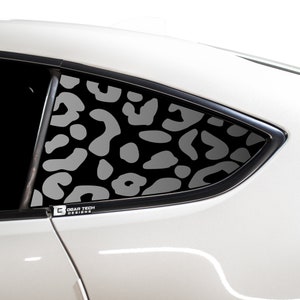 May include: A white car with a black and grey leopard print window decal. The decal is on the rear passenger side window. The decal is from the company "Bogar Tech Designs".