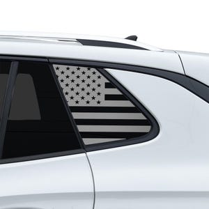 May include: A black and white American flag design is displayed on the rear passenger window of a white vehicle. The flag features black stripes and stars, creating a patriotic aesthetic. The window is framed by a black border.