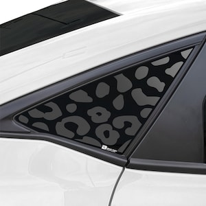 Puede incluir: Un coche blanco con un tinte de ventana de estampado de leopardo negro. El tinte está en la ventana trasera del pasajero. El coche tiene un borde negro alrededor de las ventanas.