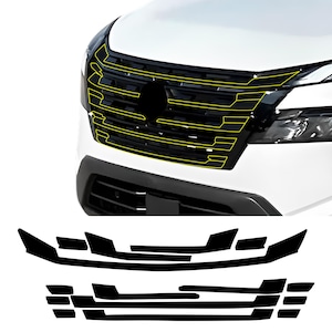 May include: A close-up of a white car's front end, showcasing a black grille with yellow accent lines. Below, black vinyl pieces are arranged, likely for customization. The car's headlights are visible.