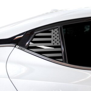 May include: A white car with a black American flag decal on the rear passenger window. The decal is a silhouette of the American flag with black stars and stripes.