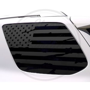 Puede incluir: Una calcomanía de bandera estadounidense desgastada en blanco y negro para la ventana de un automóvil. La bandera está ligeramente descolorida y tiene un aspecto desgastado.