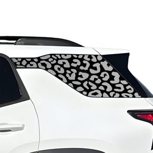 Könnte beinhalten: Ein weißes Auto mit einem schwarz-grauen Leopardenmuster-Aufkleber auf der Heckscheibe. Der Aufkleber ist ein sich wiederholendes Muster unregelmäßiger Formen. Das Rücklicht des Autos ist sichtbar.