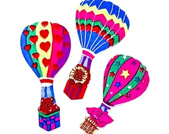 May include: Three colorful hot air balloon decorations. The left balloon features red hearts on a yellow background with a bear in the basket. The center balloon has a zigzag pattern in blue, green, and red. The right balloon is pink with stars.