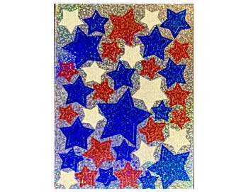May include: A rectangular sheet of stickers featuring a repeating pattern of stars in red, white, and blue. The stars are arranged in various sizes across a silver holographic background that reflects light with a shimmering, textured effect.