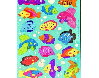 May include: A sheet of glittery stickers featuring various colorful fish on a light blue background. The fish are depicted in shades of purple, orange, pink, yellow, blue, and green. Small white circles represent bubbles, and the text 1999 Sandylion Sticker Designs is printed vertically on the right side.