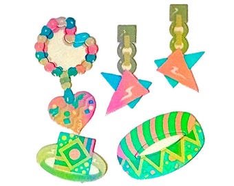 May include: A collection of colorful jewelry pieces including a heart-shaped pendant with a beaded border, two star-shaped drop earrings in pink and blue, a square-topped ring, and an oval-shaped bangle with green and orange striped patterns.
