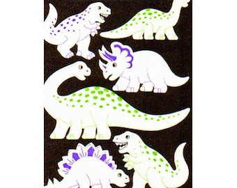 May include: A sheet of glow-in-the-dark dinosaur stickers. The stickers feature various dinosaur species in white with green or purple accents. The text "GLOW IN THE DARK" is at the top. The dinosaurs include a T-Rex, Stegosaurus, and Brontosaurus.