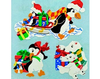 May include: A set of three die-cut stickers featuring winter animals. One shows a penguin pulling a sled with a gift, another a penguin with a red bow and a small penguin, and the third shows two polar bears holding a blue gift with a red bow.