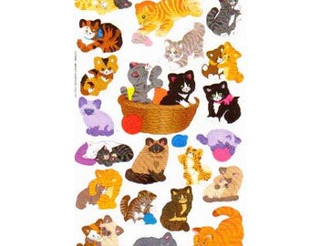 May include: A sticker sheet featuring numerous illustrations of cats in various poses and colors, including orange tabby, black, grey, and calico patterns. The cats are depicted playing with yarn, sitting in a woven basket, and cuddling together.
