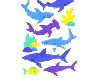 May include: A collection of foam stickers featuring various sharks in shades of blue and purple, including a hammerhead shark. The set also includes small yellow fish and colorful coral reef elements in bright green, yellow, and purple tones.