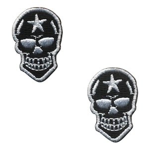 May include: Two black skull patches with white embroidered detailing. Each patch features a skull design with a star on the forehead. The patches are intricately stitched, suitable for application on clothing or accessories.