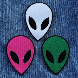 May include: Three alien head patches in different colours: white, pink and green. Each patch has black eyes and a simple alien head shape.